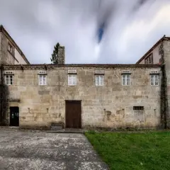 Las Torres de Allo, un edificio de piedra con un balcón ornamentado y ventanas blancas, se alza bajo un cielo nublado y dinámico.