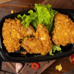 Chrupiące skrzydełka z kurczaka w panierce z płatków kukurydzianych, podane na liściach sałaty w czarnym pojemniku.