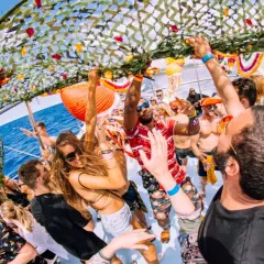Festa in barca con gente che balla sotto una rete decorata. James Jones DJ anima la folla con la sua musica.