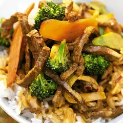 En skål med ris toppad med strimlad biff teriyaki, broccoli och morötter. En härlig asiatisk rätt.