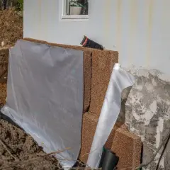 Byggarbetsplats där man ska isolera plintar med dränerande material och skyddande duk.