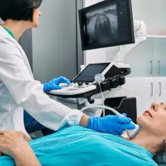 Lekarz wykonuje badanie ultrasonograficzne szyi pacjentki. Na ekranie widoczny obraz USG.