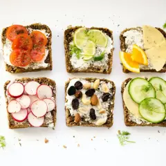 Sześć kanapek z ciemnego pieczywa z różnymi dodatkami: pomidory, limonka, ser z pomarańczą, rzodkiewki, orzechy i rodzynki, ogórek. Zdrowe jedzenie, które może pomóc w zapobieganiu zapaleniu uchyłków.