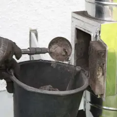 Rękawica zrzuca sadzę do wiadra. Czyszczenie komina od dołu to ważny etap dbania o bezpieczeństwo.