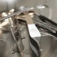 Pinces chirurgicales et fils de suture dans un plateau métallique. Un fil semble détaché, évoquant un point de suture qui a sauté après une circoncision.