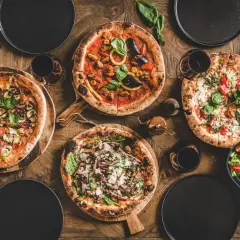 Vier Pizzen, ein Salat und Rotwein auf Holztisch. Die Frage welcher Wein zu Pizza wird hier beantwortet.