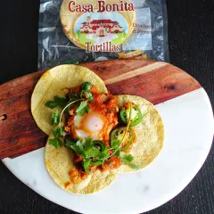 Délicieux huevos rancheros recette sur tortillas, garni d'un œuf coulant, sauce tomate épicée, jalapeños et coriandre fraîche.