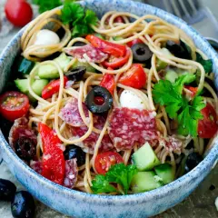Ein bunter Spaghettisalat mit Salami, Tomaten, Oliven, Gurken und Mozzarella, verfeinert mit Knoblauch und Parmesan.