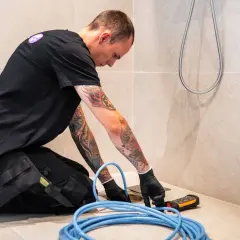 En rörmokare med tatueringar arbetar med en spolbil. Kostnad för spolbil kan variera beroende på problem.
