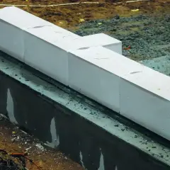 Białe bloczki z betonu komórkowego, prawdopodobnie do budowy fundamentów, leżą na warstwie izolacji. Nivoplan zapewnia stabilność konstrukcji.