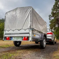 Srebrny samochód z przyczepą na leśnej drodze. Manewrowanie z przyczepą wymaga wprawy.