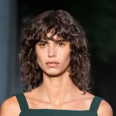 Modelo con cabello castaño ondulado y flequillo rizado, luciendo un vestido verde oscuro.