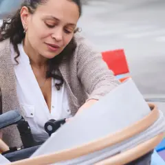 Kobieta po czterdziestce pochyla się nad wózkiem, przygotowując pierwsze dziecko do spaceru.
