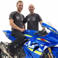 Davey Todd y su equipo posan junto a una moto Suzuki azul brillante.