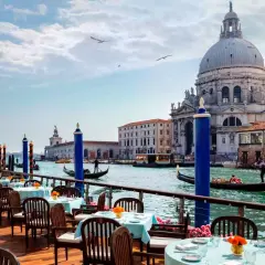 Tavoli apparecchiati su una terrazza con vista sul Canal Grande, gondole e la Basilica di Santa Maria della Salute. Un'ambientazione da sogno per i migliori ristoranti di Venezia.