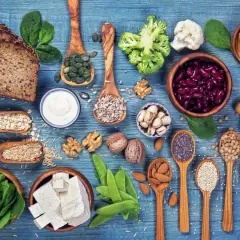 Różnorodne produkty roślinne: pieczywo, warzywa, nasiona, orzechy, fasola, tofu, na niebieskim tle.