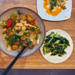 Ein Teller mit Nudeln, Kartoffeln und Gemüse, daneben ein Schälchen mit Gurkensalat. Typisch chinesisches Essen, das zum Genießen einlädt.