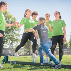 Junge Menschen üben auf einem Slackline-Parcours. Eine Dozentin unterstützt sie bei der physiotherapeutischen Ausbildung nebenberuflich.