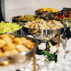 Stół z cateringiem: naleśniki, sałatka, smażone przekąski, dekoracje z kwiatów i białych kamieni.