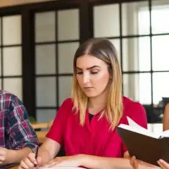 Tre studenti studiano insieme, affrontando parole difficili in inglese. Uno legge un libro, un altro scrive, il terzo analizza documenti.