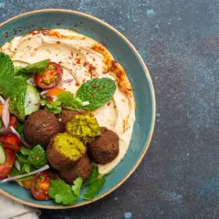 Pyszny falafel co to? Kulki z ciecierzycy z hummusem, świeżymi warzywami i miętą na talerzu.