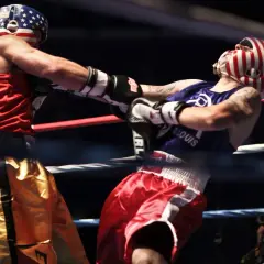 Boxer in red shorts lands a punch to the solar plexus of his opponent in red and white striped headgear.