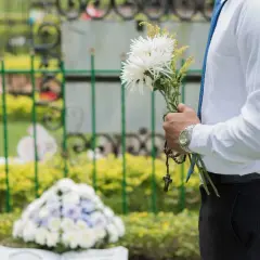 Mężczyzna w białej koszuli i niebieskim krawacie trzyma bukiet białych kwiatów i różaniec. To jego urlop okolicznościowy śmierć szwagra.