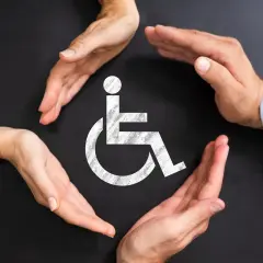 Symbol wózka inwalidzkiego otoczony dłońmi. Zatajenie niepełnosprawności przed pracodawcą może prowadzić do trudnych konsekwencji.