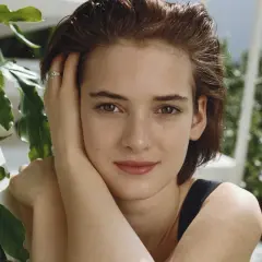 Winona Ryder joven, con su mano en la mejilla y un anillo discreto, rodeada de vegetación exuberante.