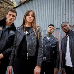 Quatre jeunes posent devant un mur en tôle ondulée, portant des vestes en cuir noir. L'un d'eux arbore une veste cuir mouton avec un col en fourrure.