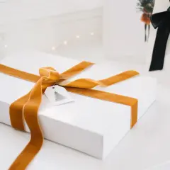 Ett vitt paket med gyllene sammetsband, ett sätt att slå in paket utan tejp. En julklapp med en liten etikett med gran.