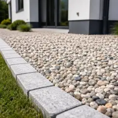 Nowy, nowoczesny dom otoczony jest żwirową ścieżką, która stanowi estetyczną opaskę wokół domu.