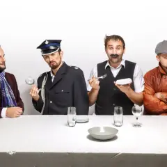 Czterech panów przy stole, jeden w garniturze, drugi w mundurze, trzeci z wąsami i sztućcami, czwarty w skórzanej kurtce. Scena jak z kabaretu z Kielc.