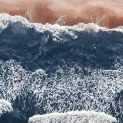 Widok z lotu ptaka na plażę i ciemne morze z kilkoma pływającymi ludźmi.