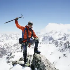 Szczęśliwy alpinista na szczycie, z lodowym toporem w dłoni, podziwia majestatyczne szczyty górskie.