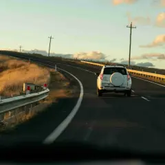 Biały SUV jedzie pustą drogą w Australii, otoczoną złotymi trawami i słupami telegraficznymi. Ruch drogowy jest minimalny.