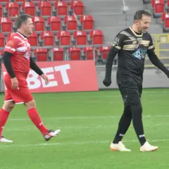 Dwóch piłkarzy, jeden w czerwonej koszulce z numerem 9, drugi w czarnej, idzie po boisku.
