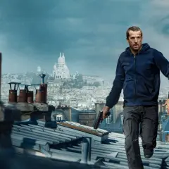 Ad vitam obsada: mężczyzna z pistoletem biegnie po dachach Paryża, w tle widoczna bazylika Sacré-Cœur i twarz kobiety.