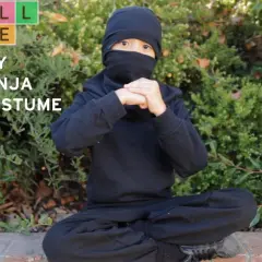 Dziecko w czarnym stroju ninja siedzi na ziemi, ręce złożone w geście.