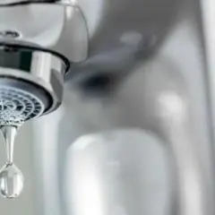 Goutte d'eau tombant d'un robinet qui goutte. Le chrome brillant du robinet contraste avec la goutte d'eau transparente.
