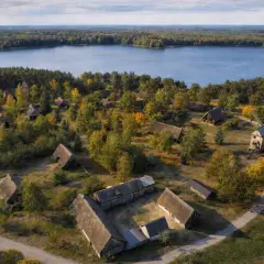 Wdzydze Kiszewskie: skansen z drewnianymi chatami i wiatrakiem nad jeziorem, otoczony jesiennym lasem.