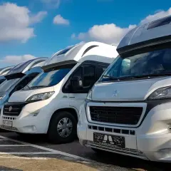 Rząd kamperów na parkingu, idealny na wakacje. Szukasz kamper tanio? Te pojazdy czekają na Ciebie!