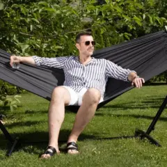 Mężczyzna w okularach relaksuje się w czarnym hamaku na stelażu. Idealny wybór, by odpocząć w ogrodzie.