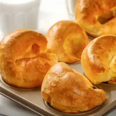 Goldbraune Yorkshire Pudding im Muffinblech, bereit für ein köstliches Rezept. Daneben ein Ei und ein Glas Milch.