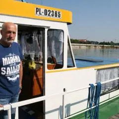 Mężczyzna na pokładzie statku, symbolizującego transport rzeczny. Widoczna tablica rejestracyjna PL-02365.