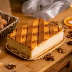 Kawałek sernika z kratką z kruchego ciasta, otoczony orzechami, mandarynkami i przyprawami.