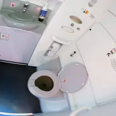 Wnętrze toalety samolotowej z umywalką i otwartą muszlą klozetową.