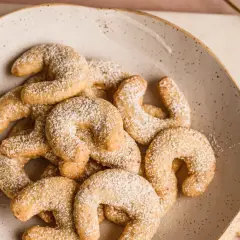 Vanillekipferl low carb, zart bestäubt mit Puderzucker, auf einem rustikalen Teller. Ein Genuss ohne Reue!