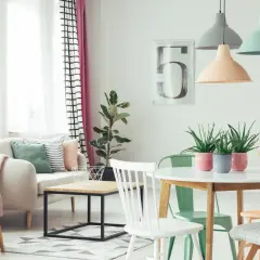 Przytulny salon z sofą i fotelem w **kolorach pastelowych**. W centralnym punkcie stoi okrągły stół z roślinami w doniczkach.