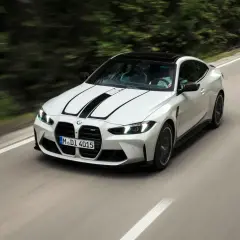 Białe BMW F82 z czarnymi pasami na masce pędzi po krętej drodze wśród zieleni.